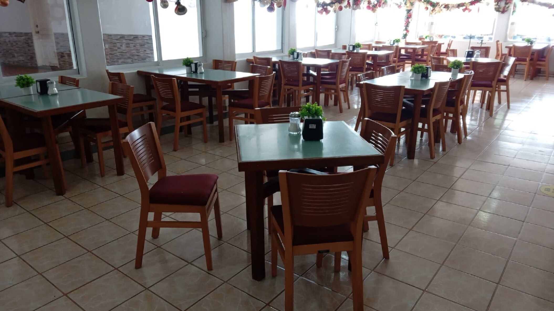 A spacious dining area with multiple tables and chairs, large windows, and a tiled floor.
