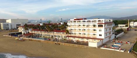 A beachfront hotel with multiple balconies, a pool area, and a beachside location.