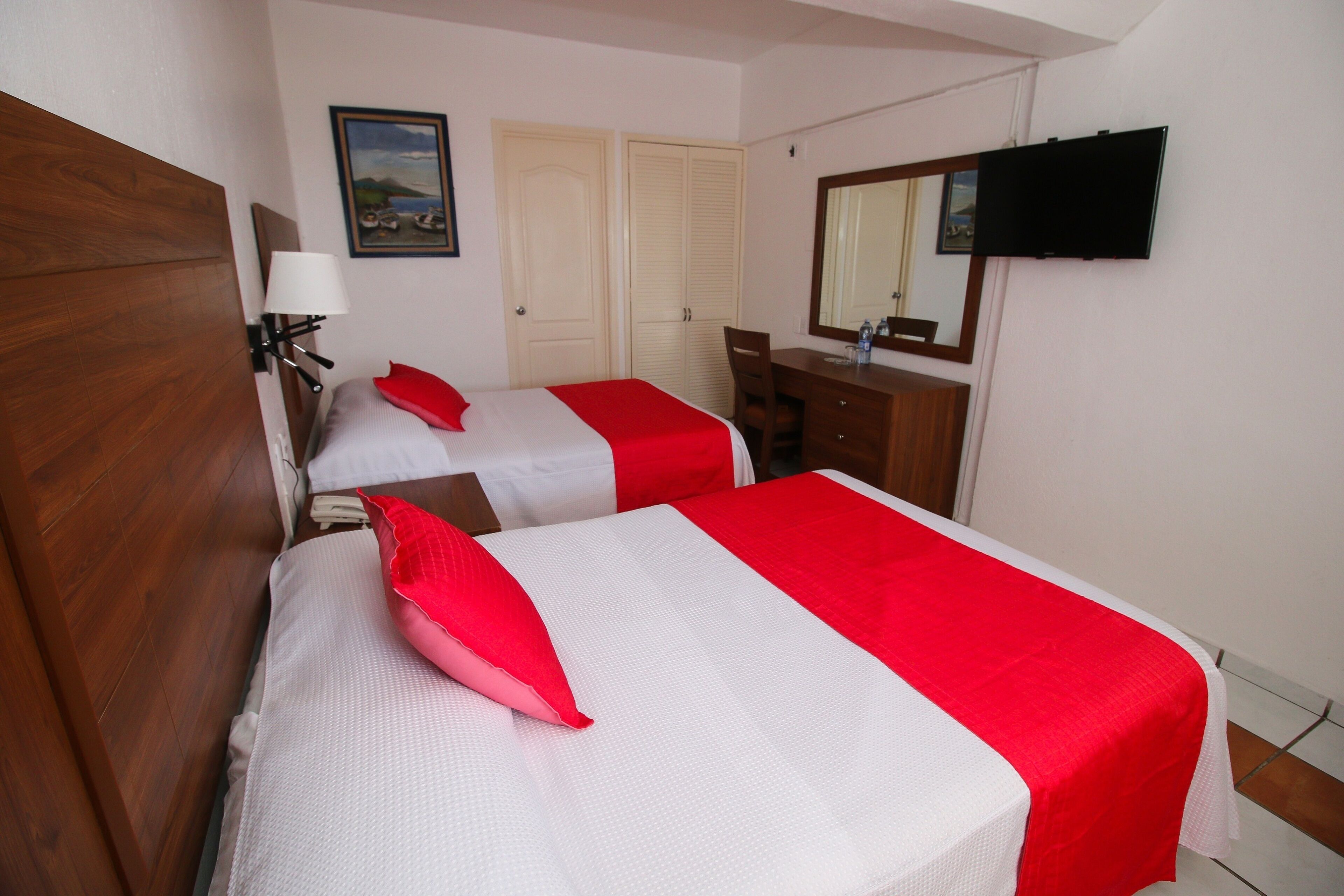 Een hotelkamer met twee bedden, een houten hoofdbord, een bureau, een stoel, een televisie en een schilderij aan de muur.