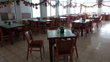 A spacious dining area with multiple tables and chairs, decorated with festive garlands.