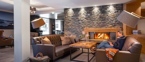 A modern living room with a stone wall, leather sofas, a fireplace, and a large window.