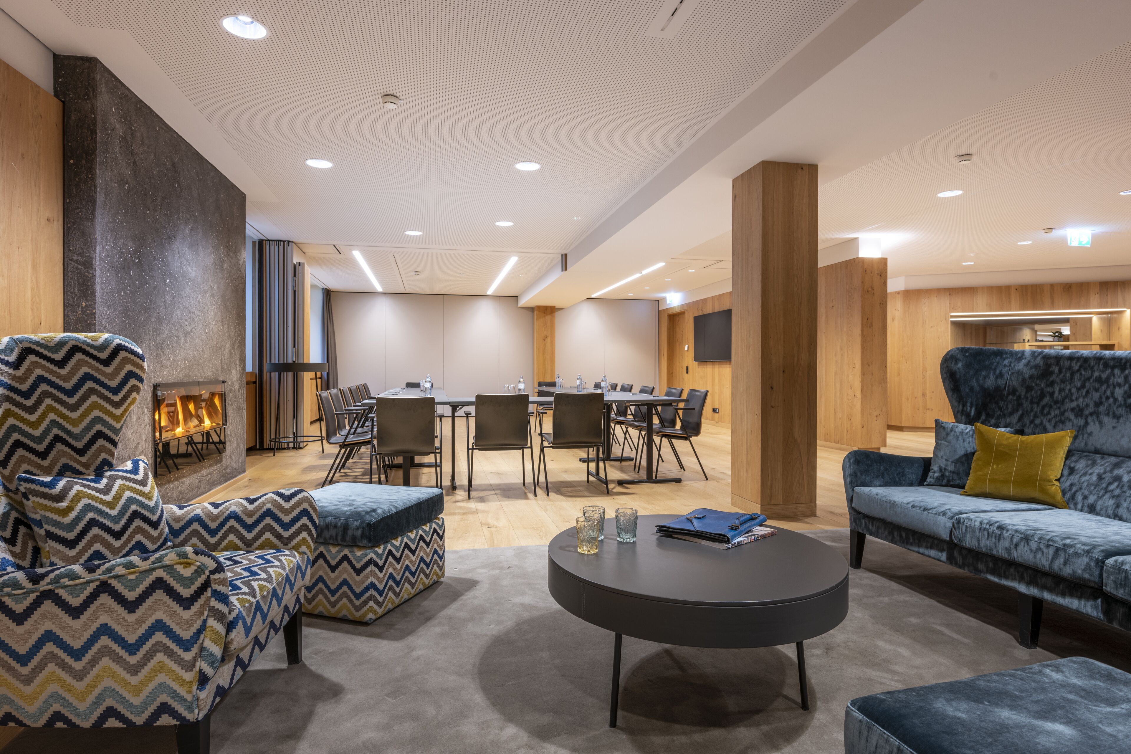 Un espace de détente moderne avec une cheminée, des sièges confortables, une table ronde et un coin cuisine en arrière-plan.