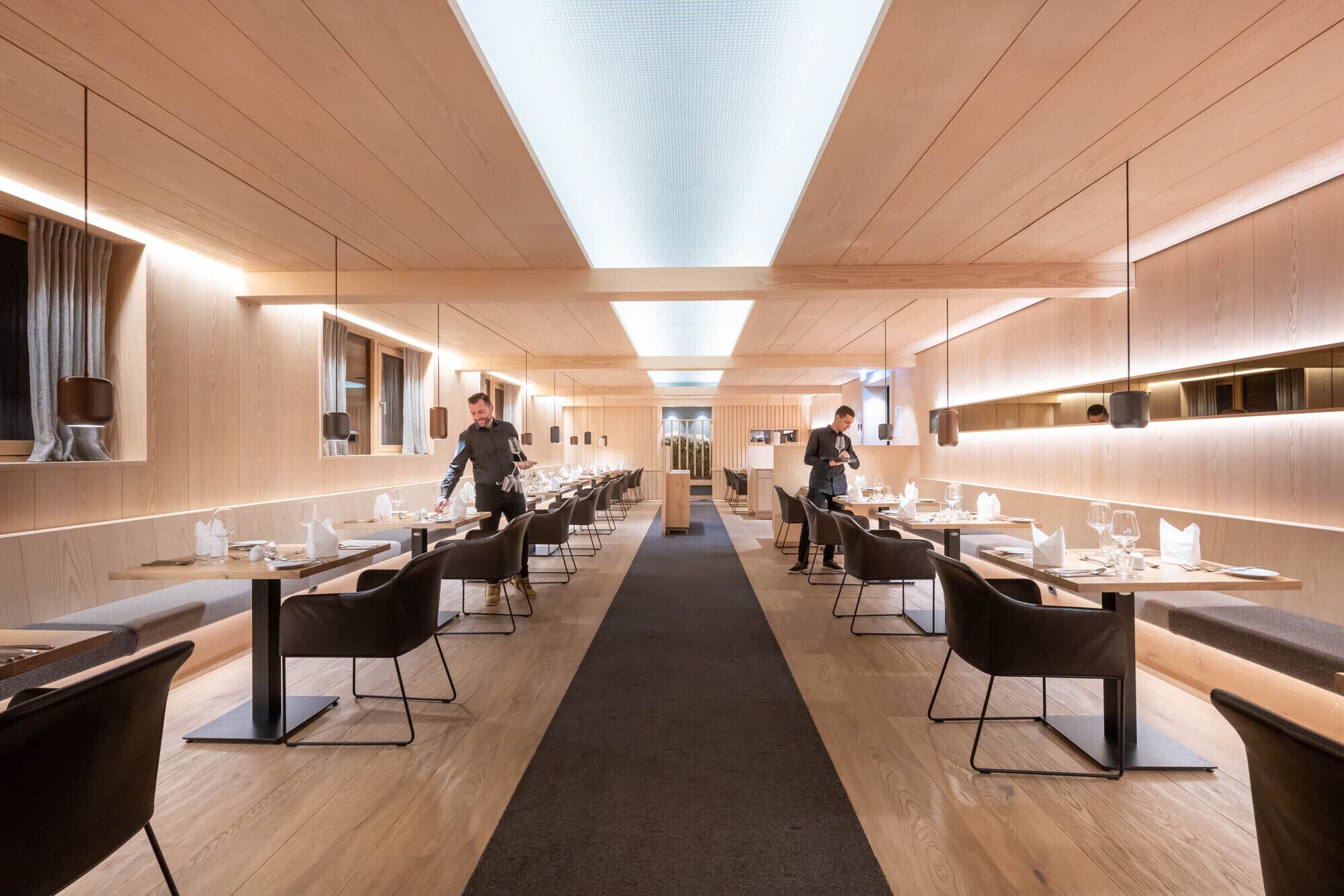Un restaurante moderno con paneles de madera, sillas negras y un pasillo central.