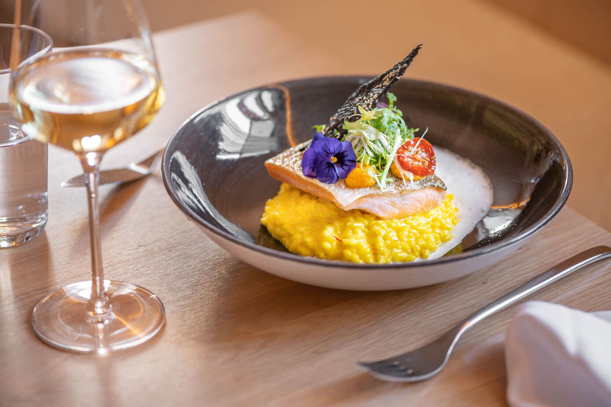 A dish with salmon, yellow risotto, and a decorative garnish on a plate.