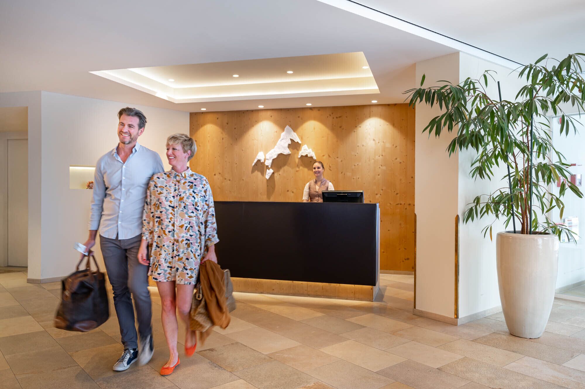 Un área de recepción con un mostrador de madera, una planta en maceta grande y un diseño moderno de techo.