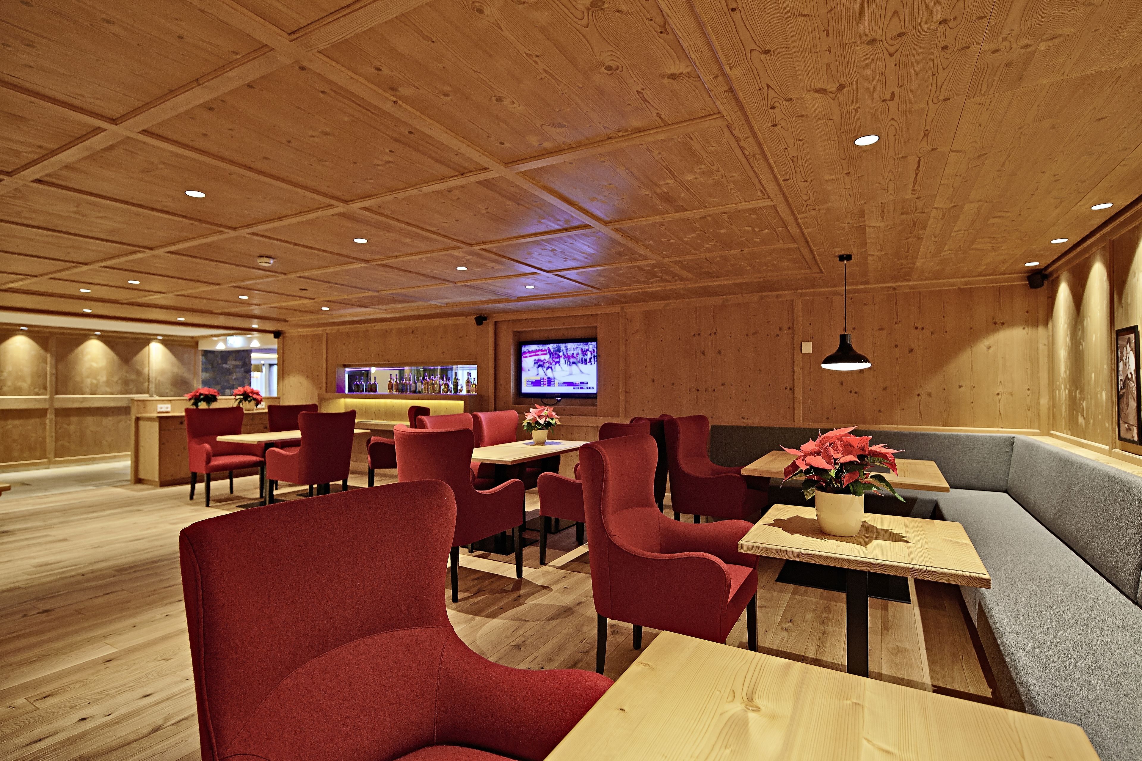 A restaurant with wooden panel walls, red upholstered chairs, and a television screen in the background.