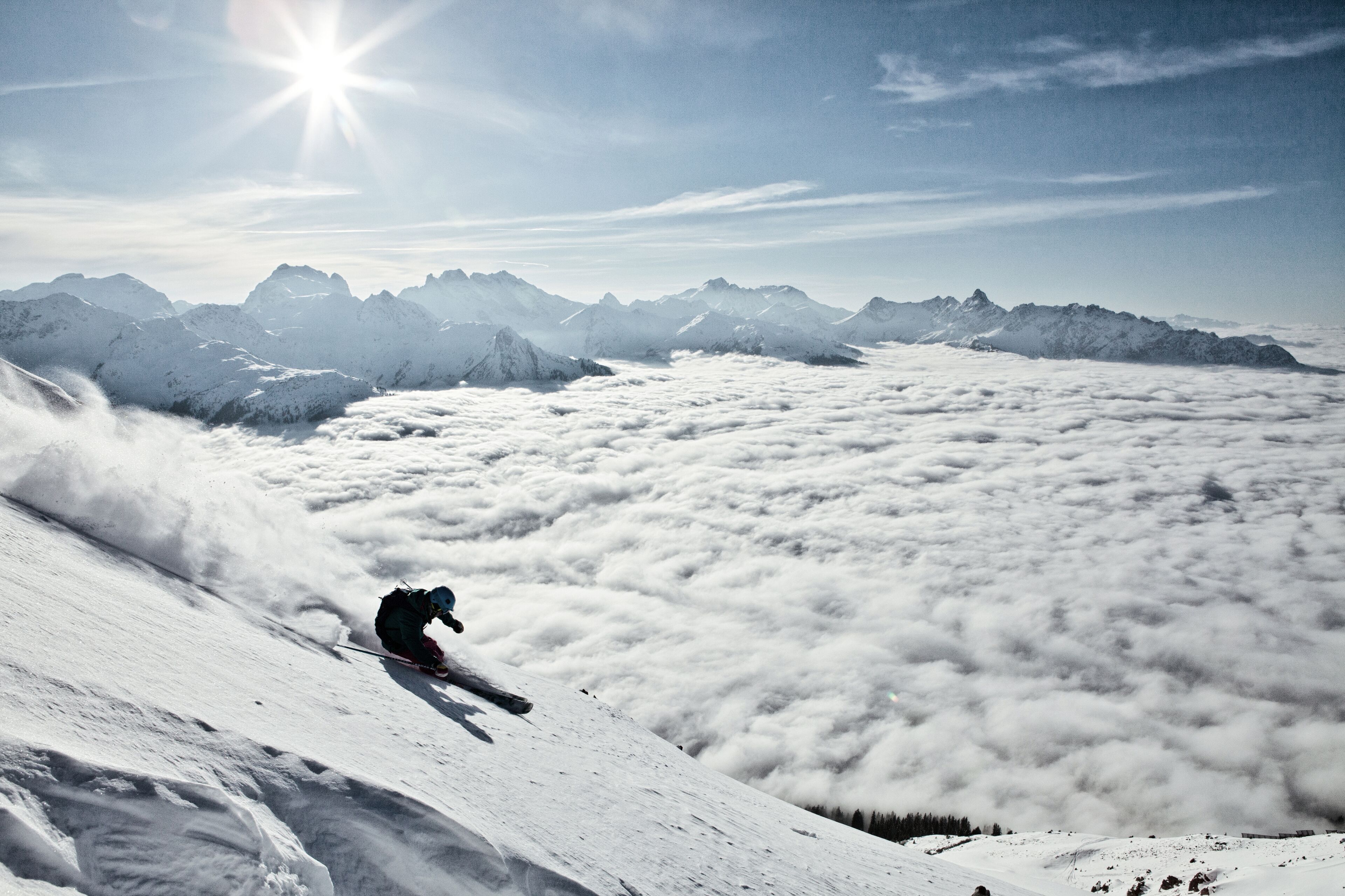A skier descending a snow-covered slope with a mountain range in the background.