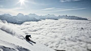 Un esquiador descendiendo una pendiente nevada con una cadena montañosa al fondo.