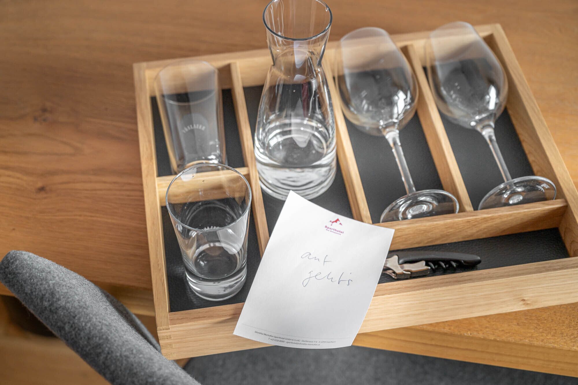 A wooden tray with wine glasses and a bottle, a napkin, and a pen.