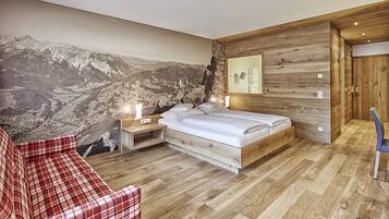 Quarto com cama grande, sofá vermelho xadrez, piso de madeira e painel mural com paisagem de montanhas.