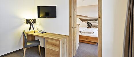 A bedroom with a wooden desk, a chair, a bed, and a TV mounted on the wall.