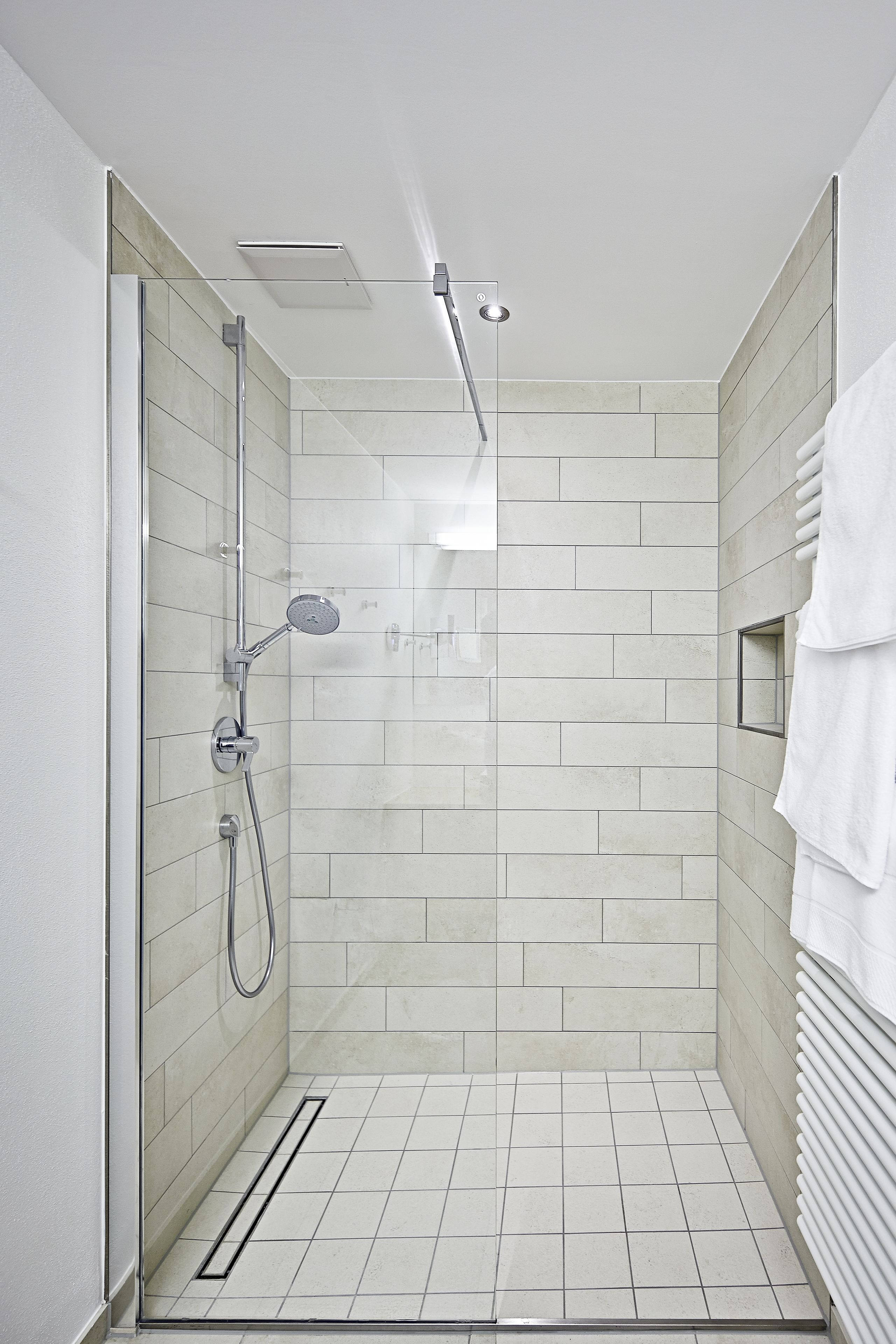 A modern shower with a glass door, a handheld showerhead, and a wall-mounted faucet.