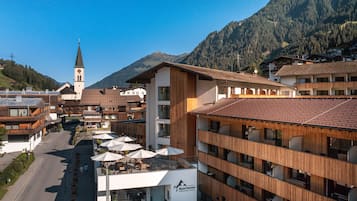Un hotel de diseño moderno, con una vista destacada de la montaña, una iglesia al fondo y mesas exteriores con sombrillas.