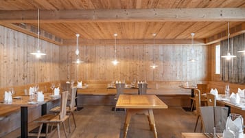 Ein Restaurant mit Holzwänden und -decken, mehreren Tischen und Bänken sowie Pendelleuchten.