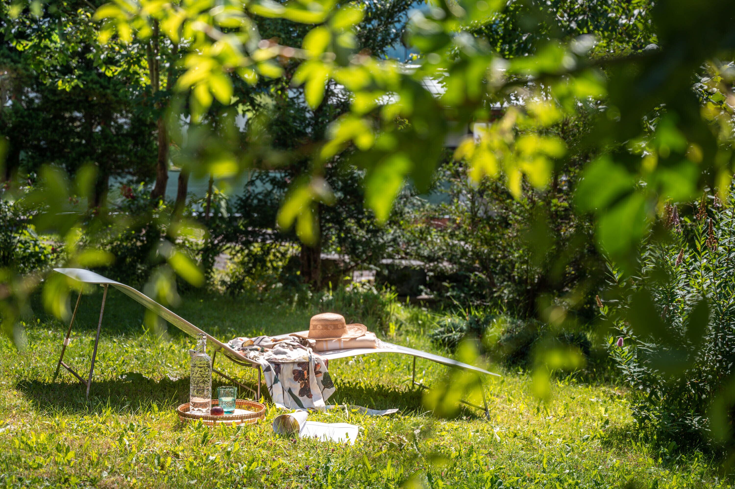 A picnic setup with a table, a hat, a bottle, and glasses on a grassy area.
