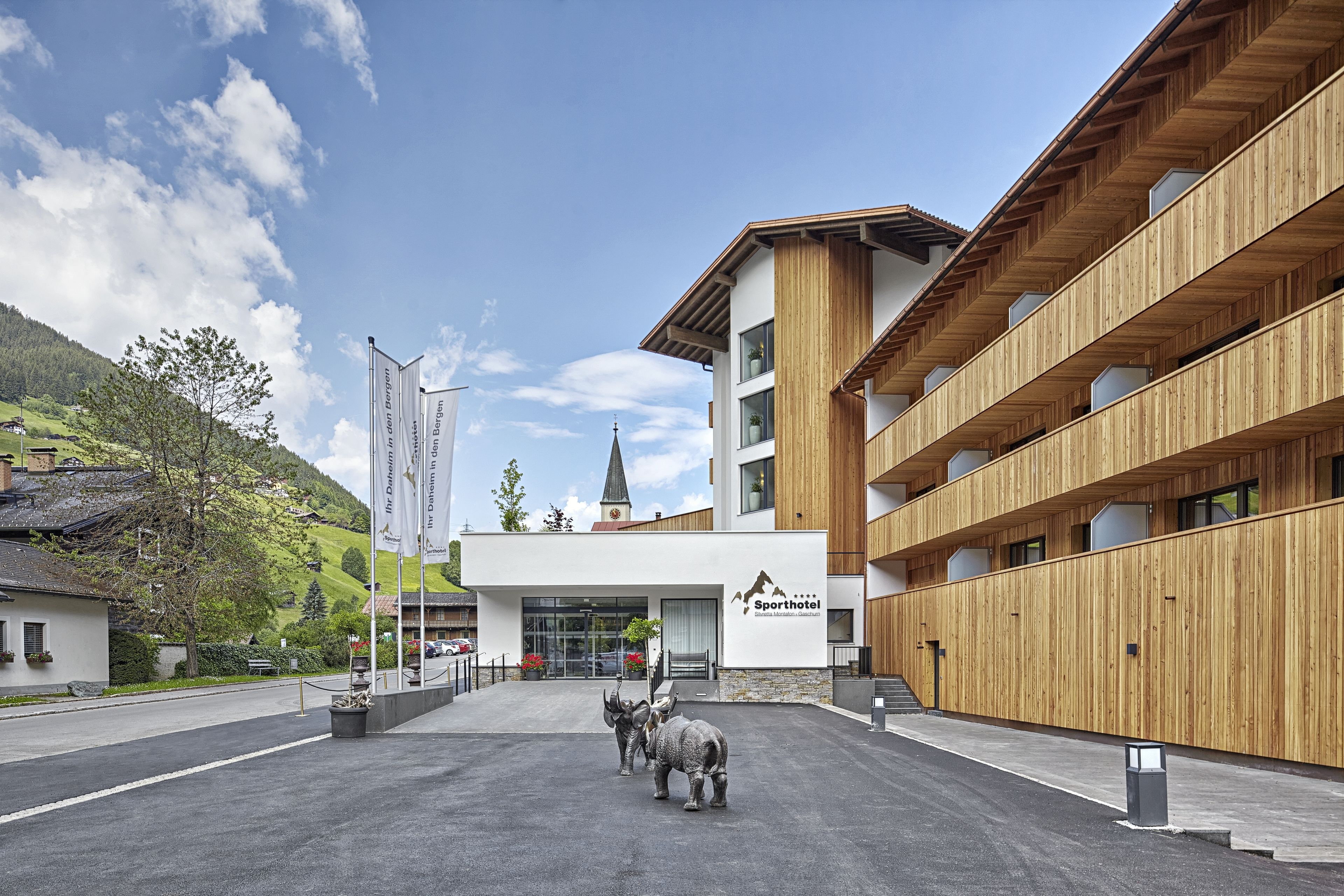 A modern hotel with a wooden facade, a central entrance, and a mountain view.