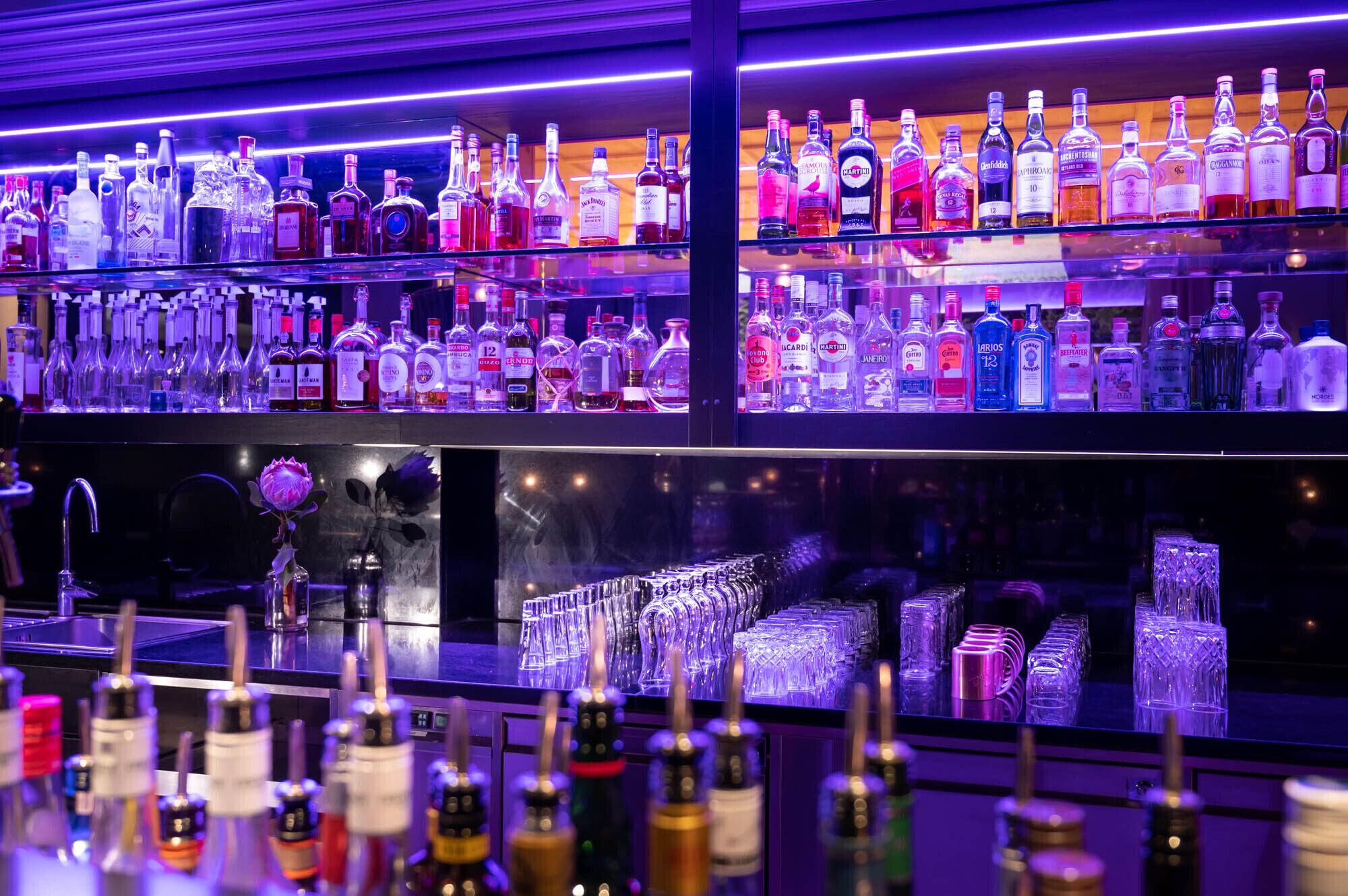 Un bar con estantes llenos de botellas de licores y una variedad de copas.