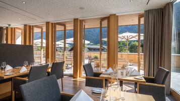 Un restaurante con mesas y sillas de madera, grandes ventanales y vistas a las montañas.