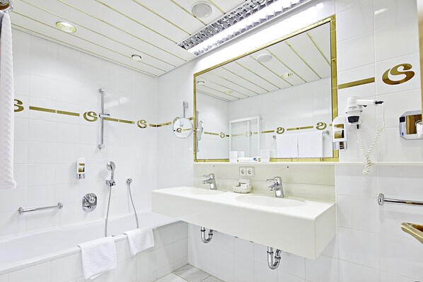 A modern bathroom with a large mirror, two sinks, a bathtub, and a towel rack. - Sporthotel Silvretta Montafon (Gaschurn)