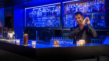 Un bar con un cantinero preparando bebidas, estantes con botellas de licores y un interior bien iluminado.