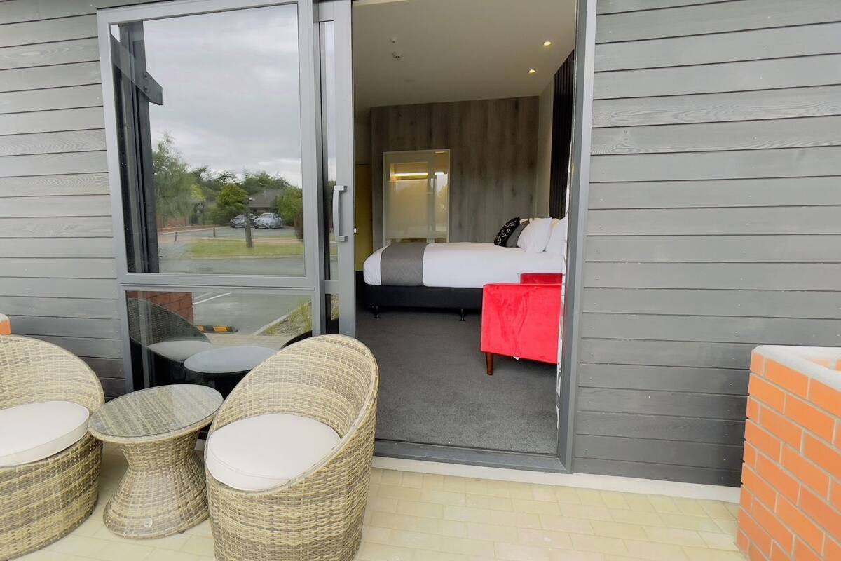 Ein Hotelzimmer mit einem Bett, einem roten Sessel und Korbmöbeln vor der Tür.