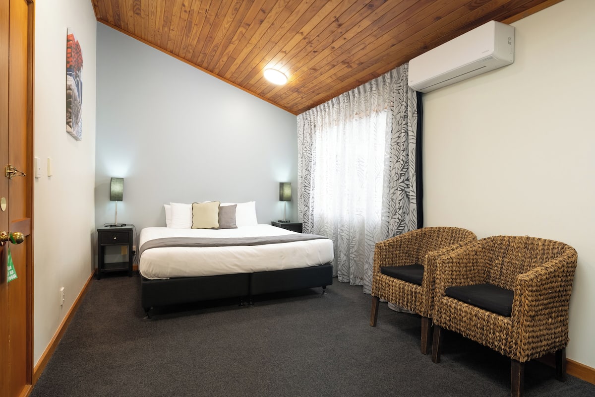 Ein Schlafzimmer mit einem Bett, zwei Nachttischen, einem Sessel und einer Klimaanlage.
