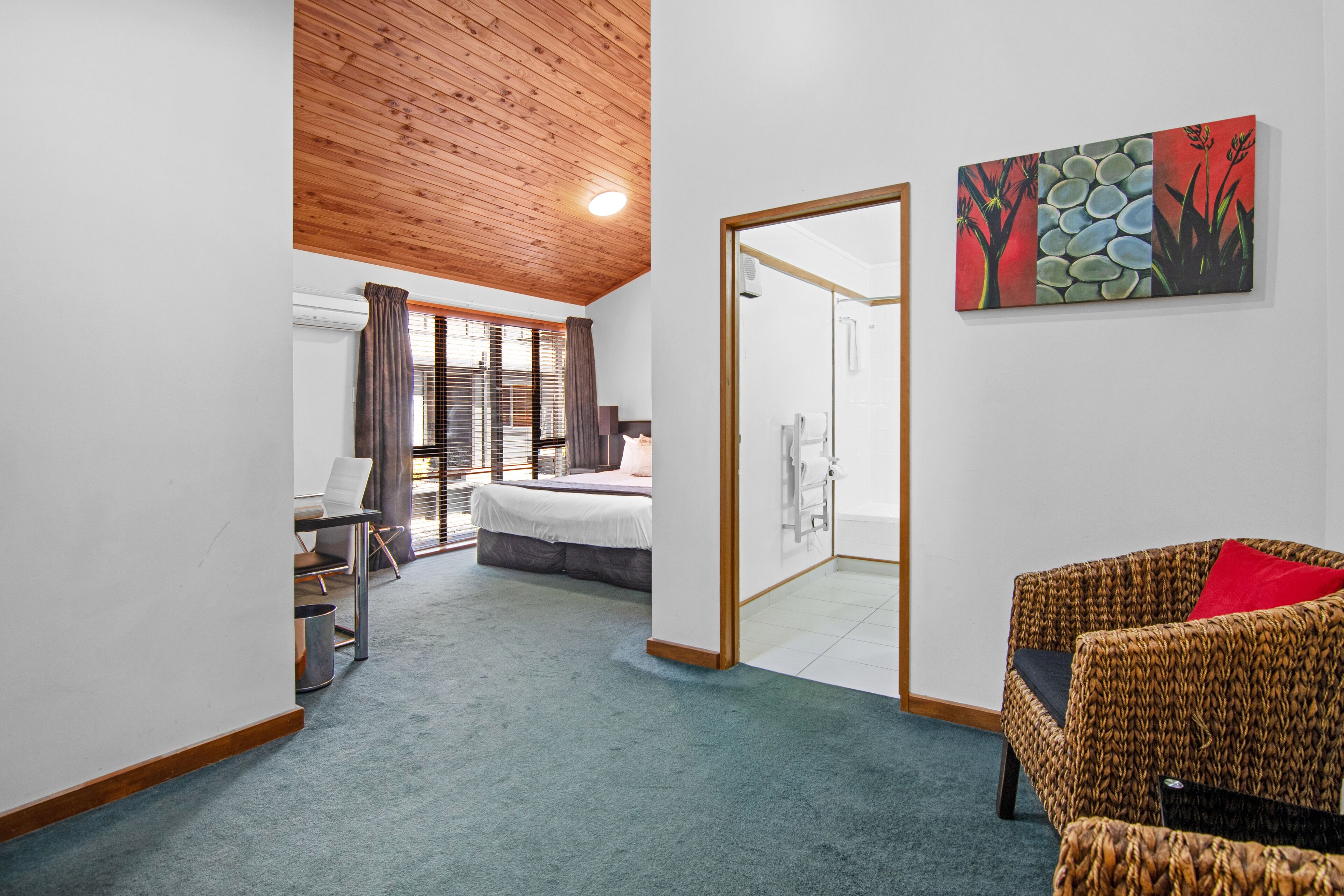 A room with a bed, a desk, a chair, and a sofa. There is a painting on the wall and a door leading to a bathroom.