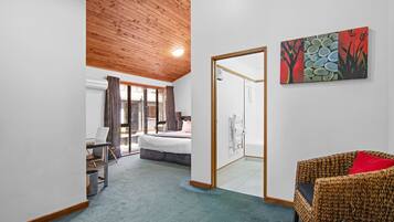 A room with a bed, a desk, a chair, and a sofa. There is a painting on the wall and a door leading to a bathroom.