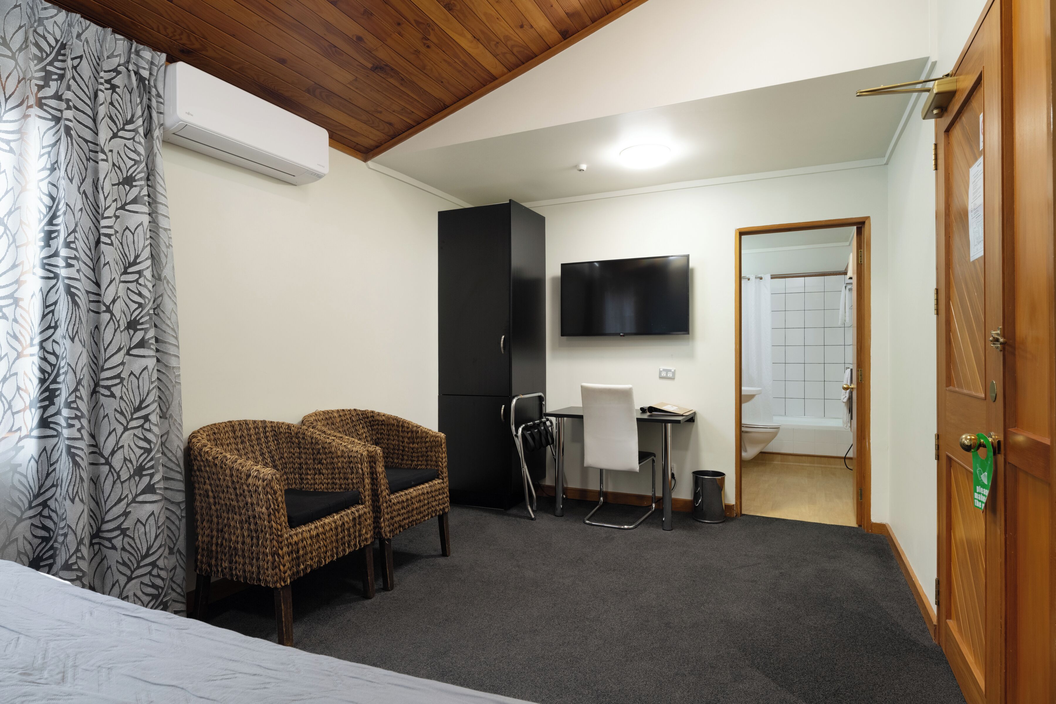 A room with two wicker chairs, a desk, a flat-screen TV, and a shower area.