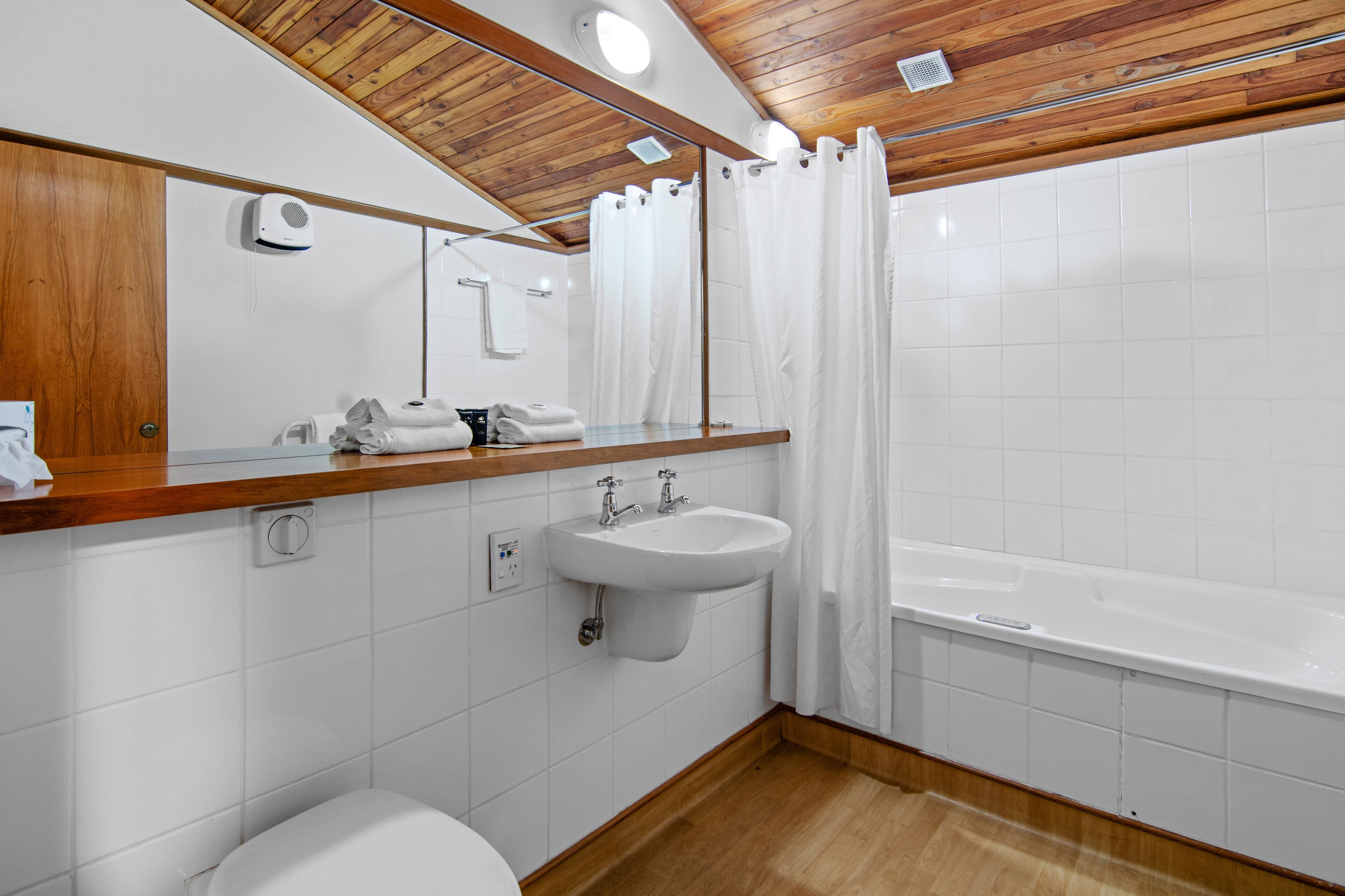 A modern bathroom with a wooden ceiling, white tiles, a sink, a toilet, and a bathtub.