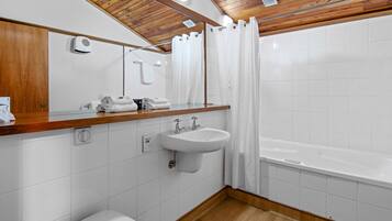 A modern bathroom with a wooden ceiling, white tiles, a sink, a toilet, and a bathtub.