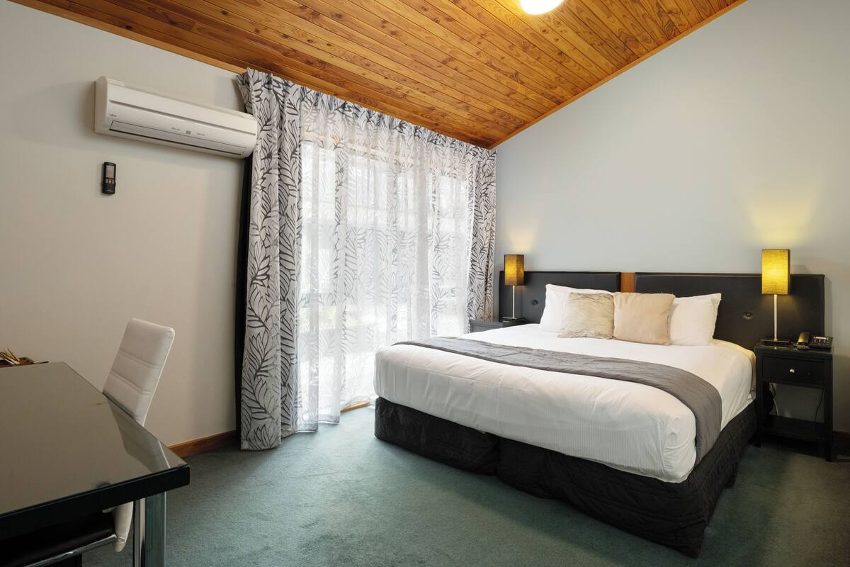 Ein Schlafzimmer mit Bett, Nachttischen, einem Schreibtisch und einer Klimaanlage.