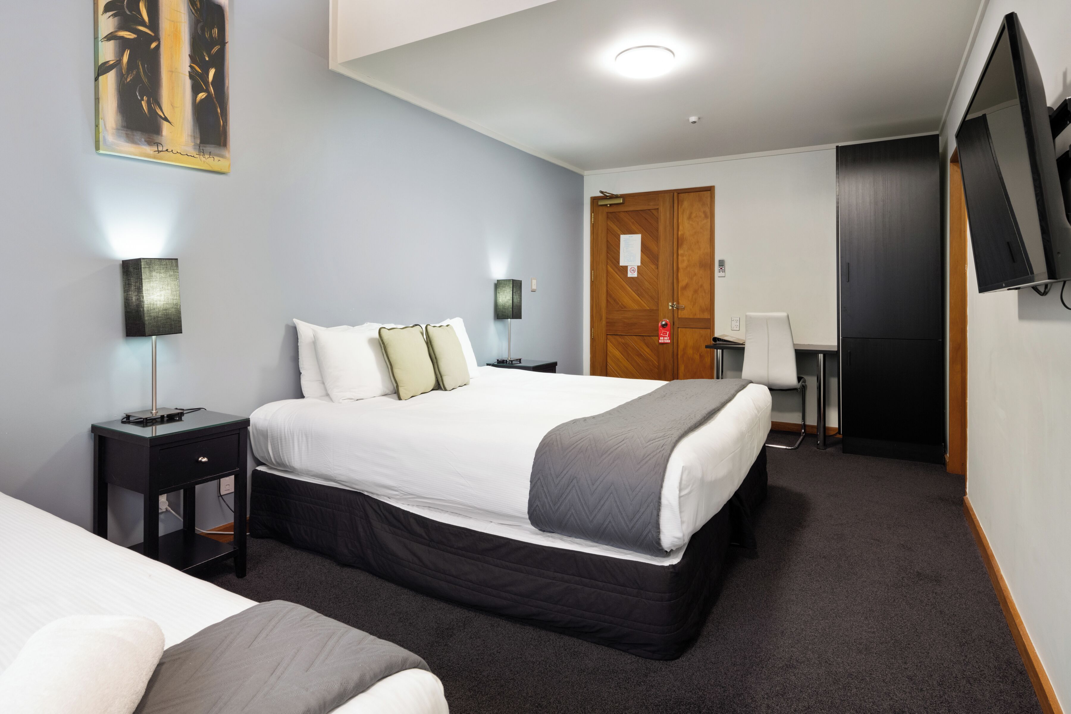 A hotel room with a bed, bedside tables, a desk, a chair, a television, and a door.