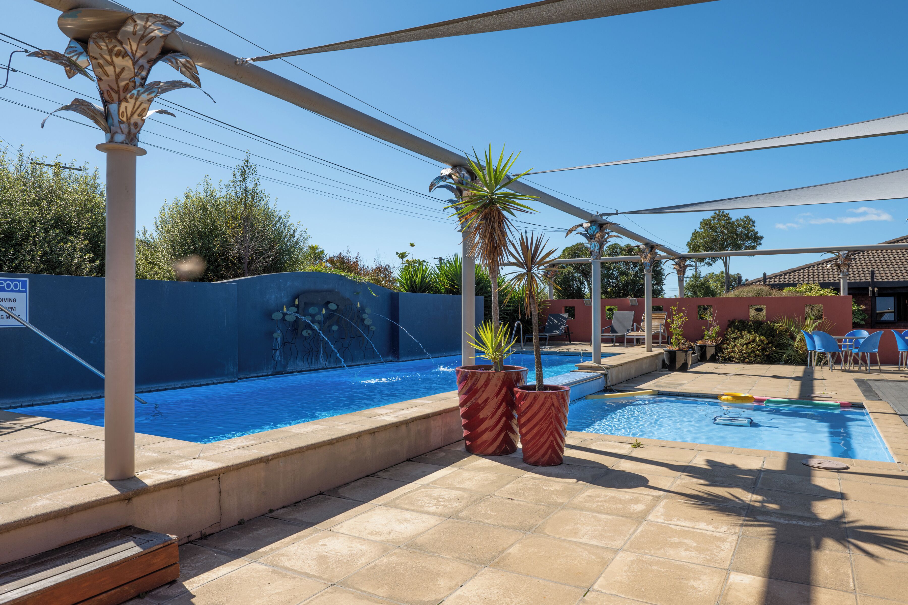 Un espace piscine agrémenté d’un élément décoratif aquatique, de plantes en pot et de mobilier d’extérieur.