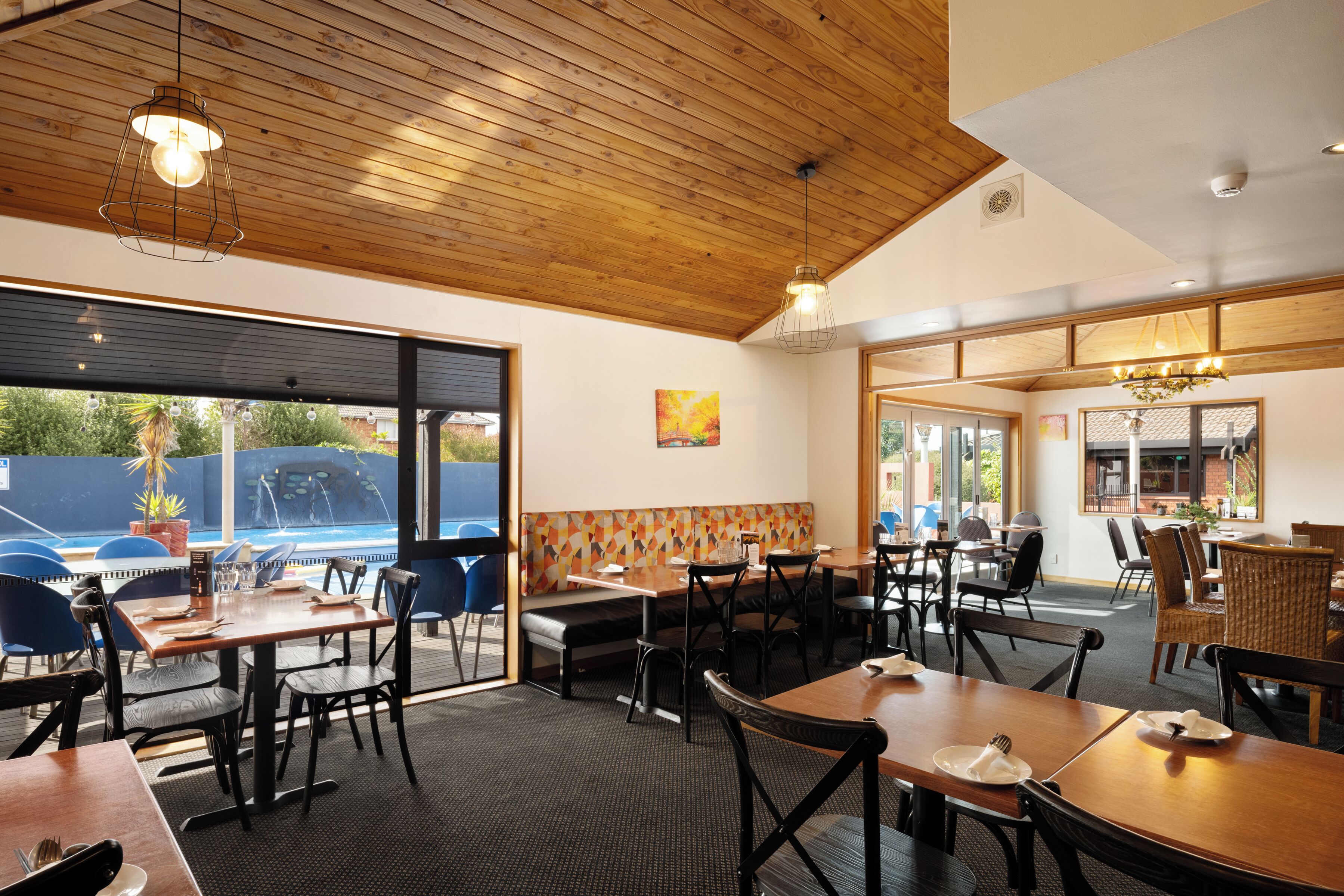 A restaurant with wooden ceiling, large windows, and a pool view.