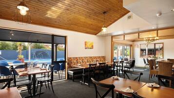 A restaurant with wooden ceiling, large windows, and a pool view.