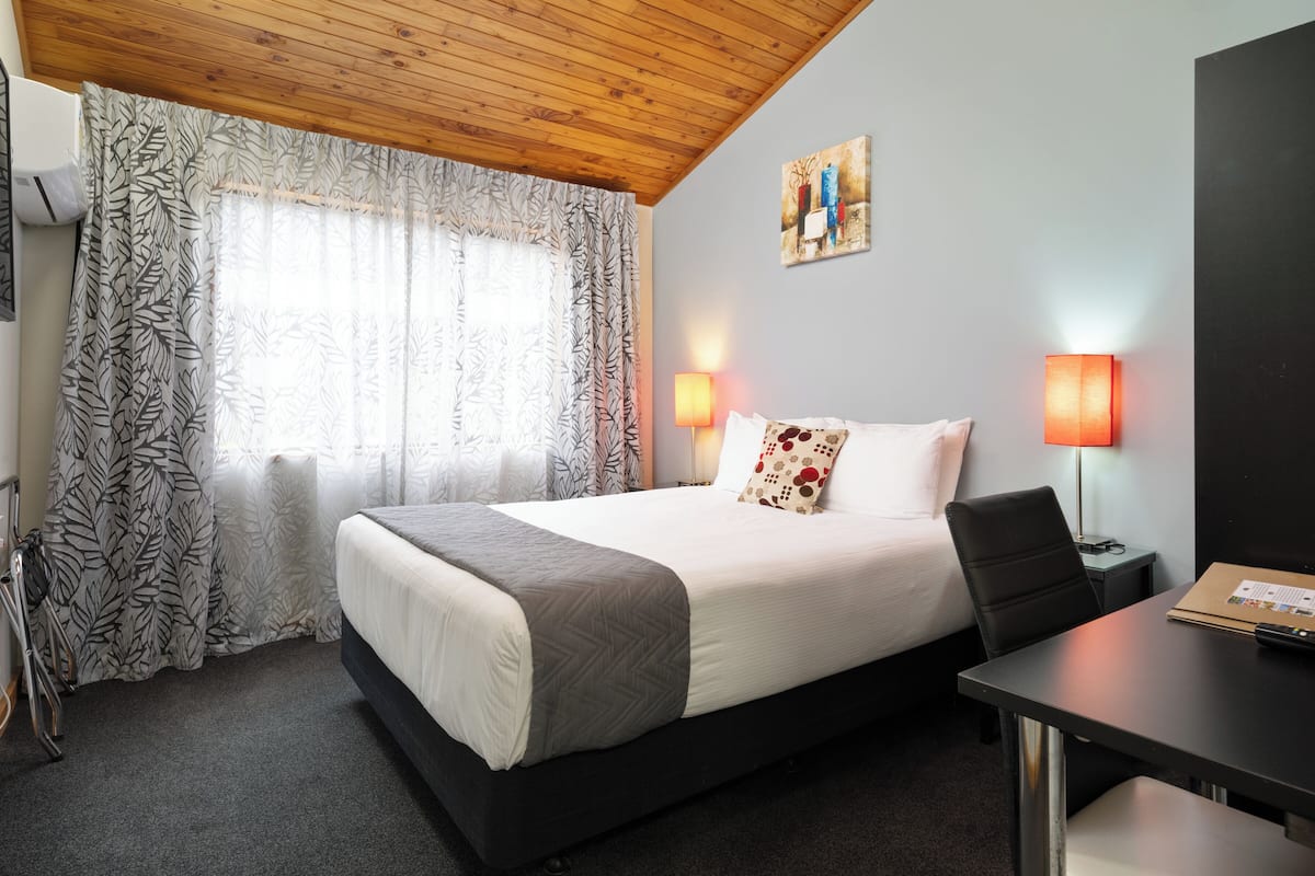 Ein Hotelzimmer mit einem Bett, zwei Nachttischlampen, einem Schreibtisch und einem Stuhl.