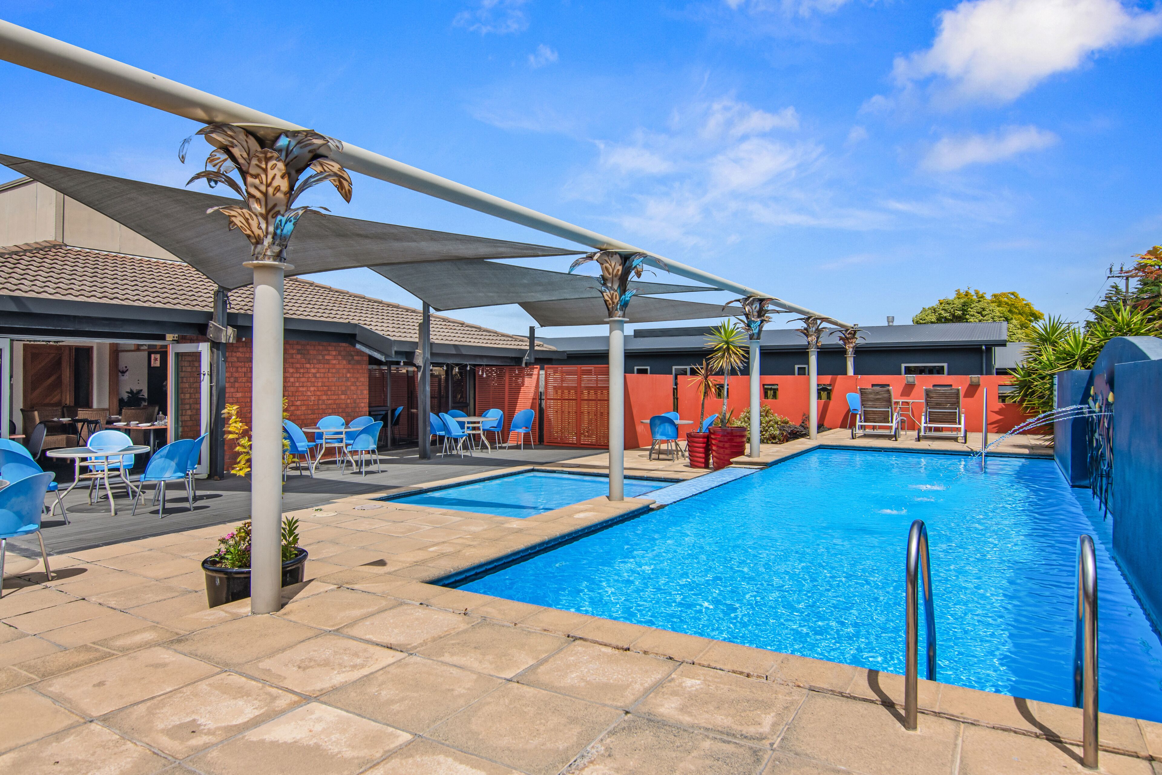 Une piscine avec un parasol, des chaises bleues et un bâtiment en briques en arrière-plan.