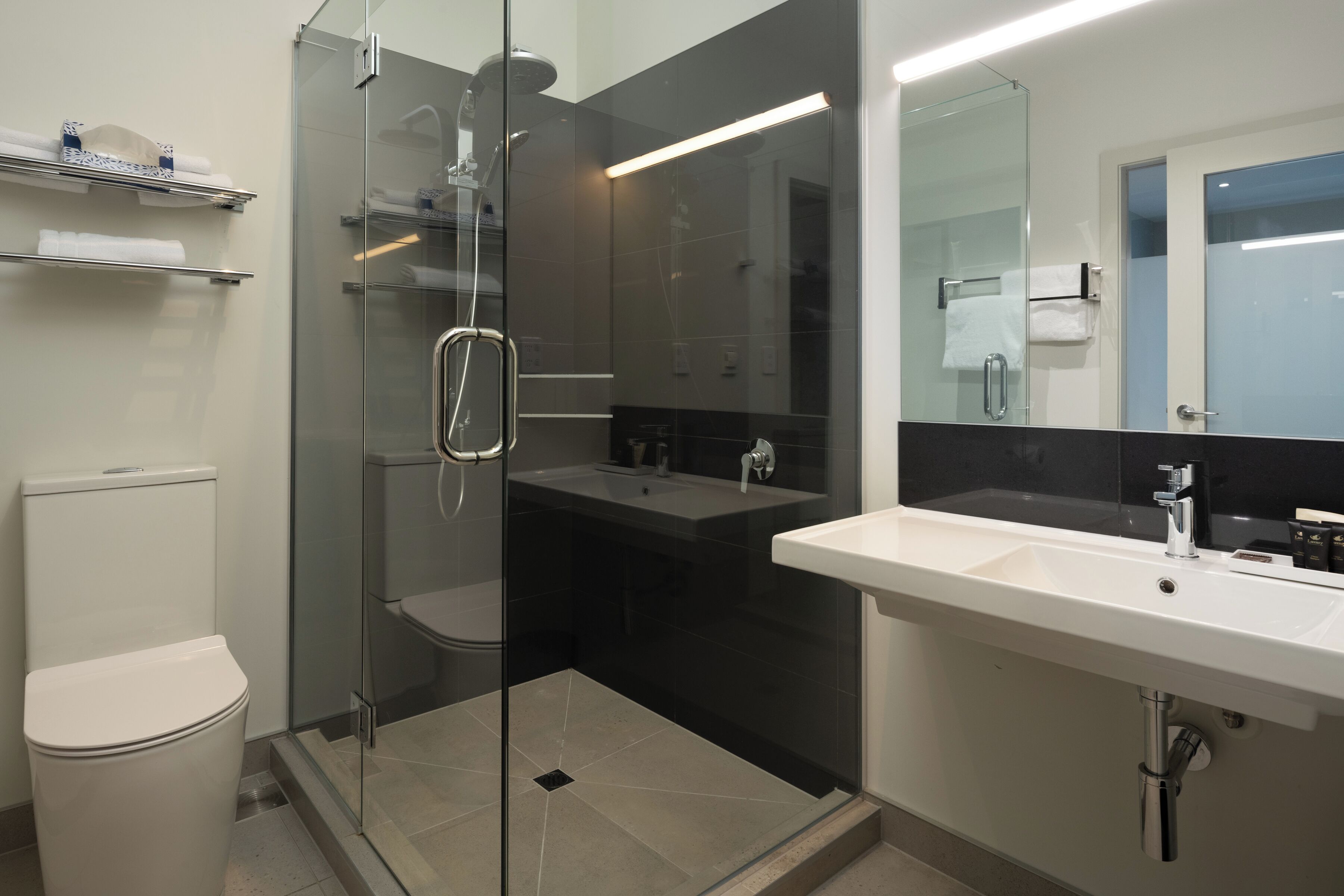 Un bagno moderno con doccia vetro, lavabo bianco e water.