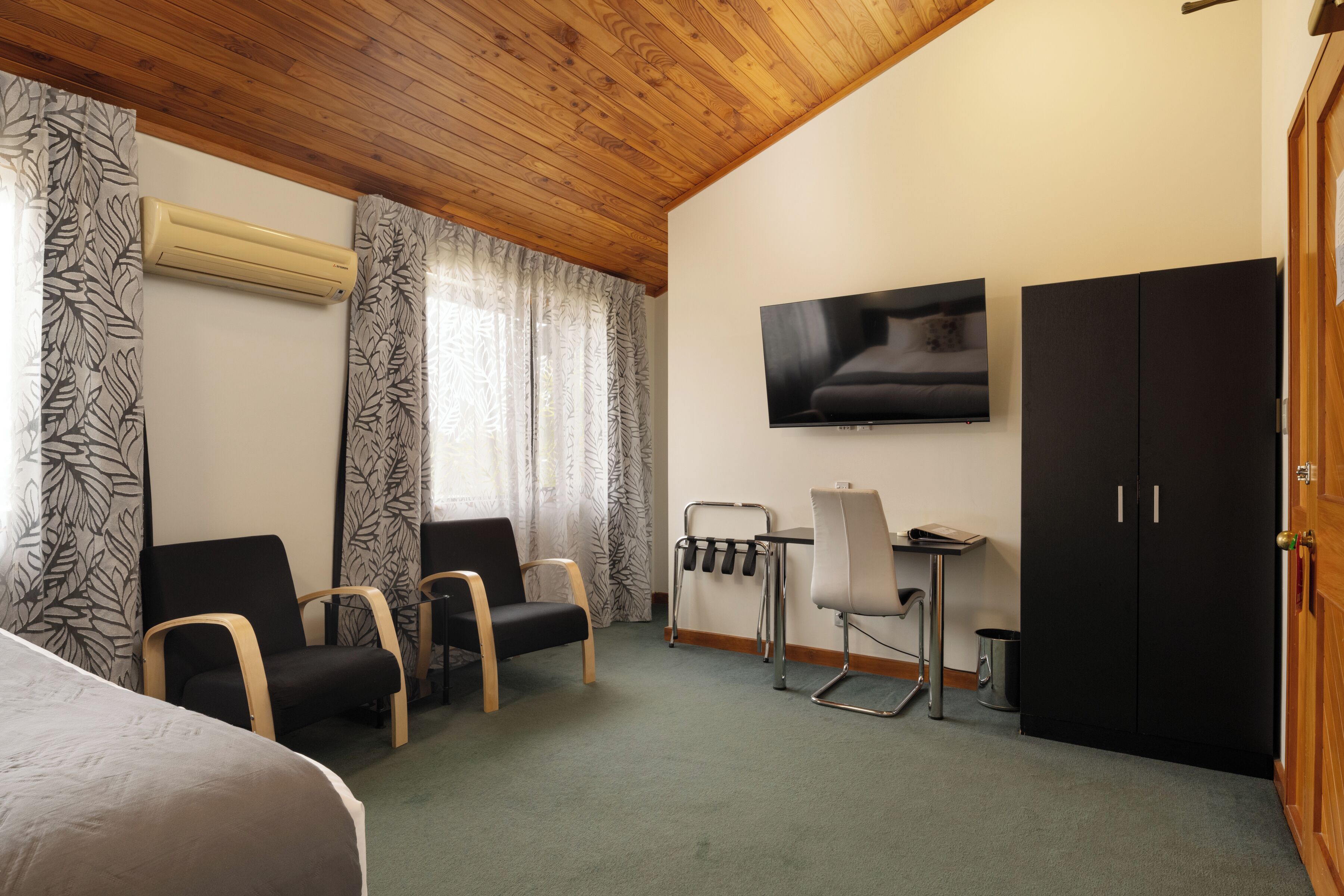 Une chambre d’hôtel comprenant un lit, deux chaises, un bureau avec une chaise, une télévision et une armoire.