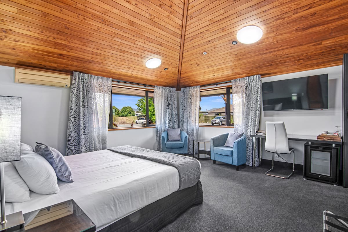 Ein Schlafzimmer mit einem großen Bett, zwei Sesseln, einem Schreibtisch und einem Fernseher.