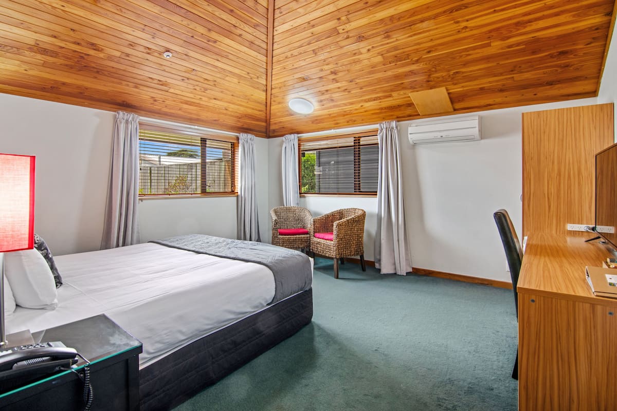 Ein Hotelzimmer mit Holzboden, einem Bett, einem Schreibtisch, einem Stuhl und einem Vorhangfenster.
