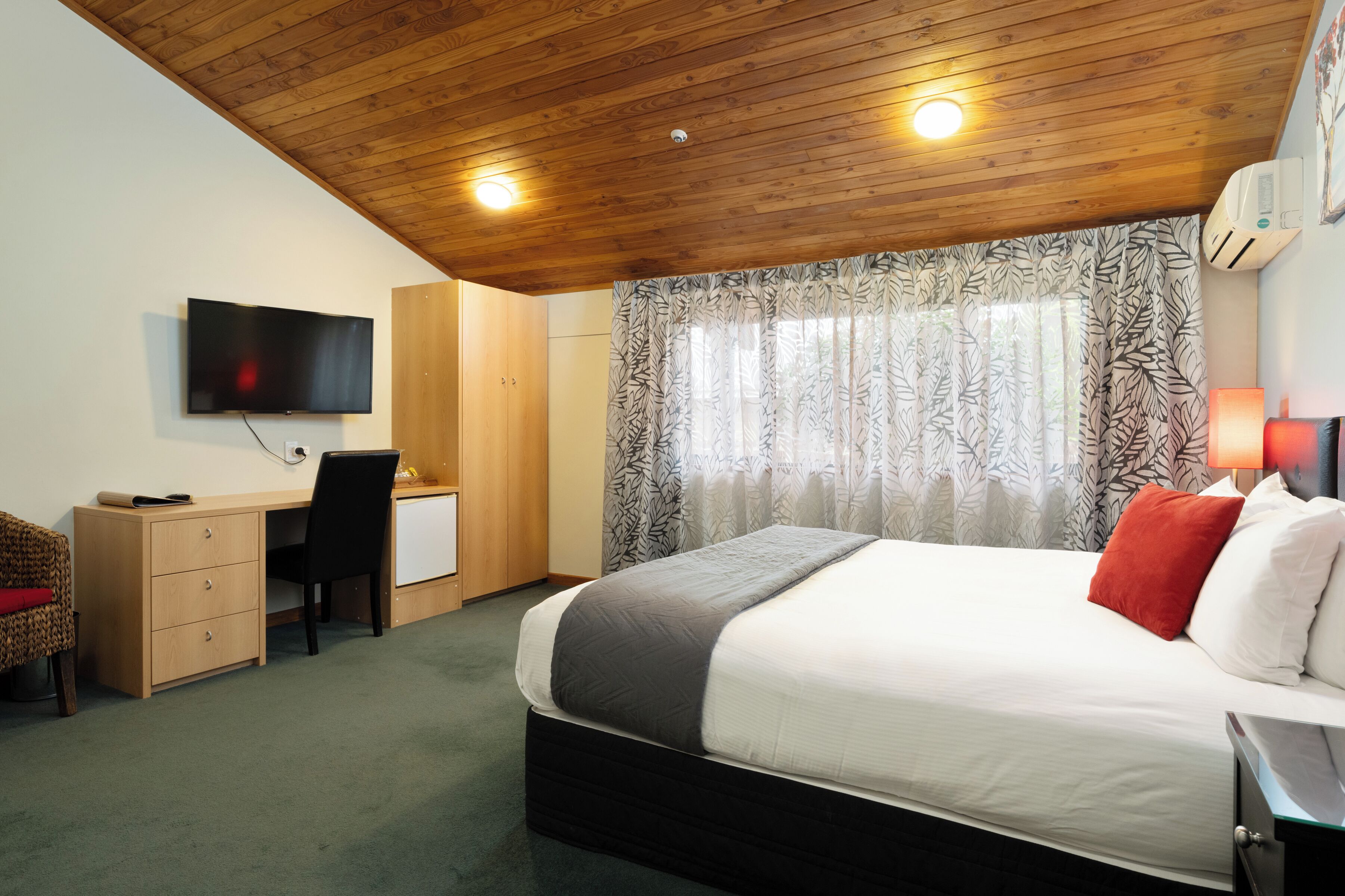 A bedroom with a bed, desk, chair, and TV.