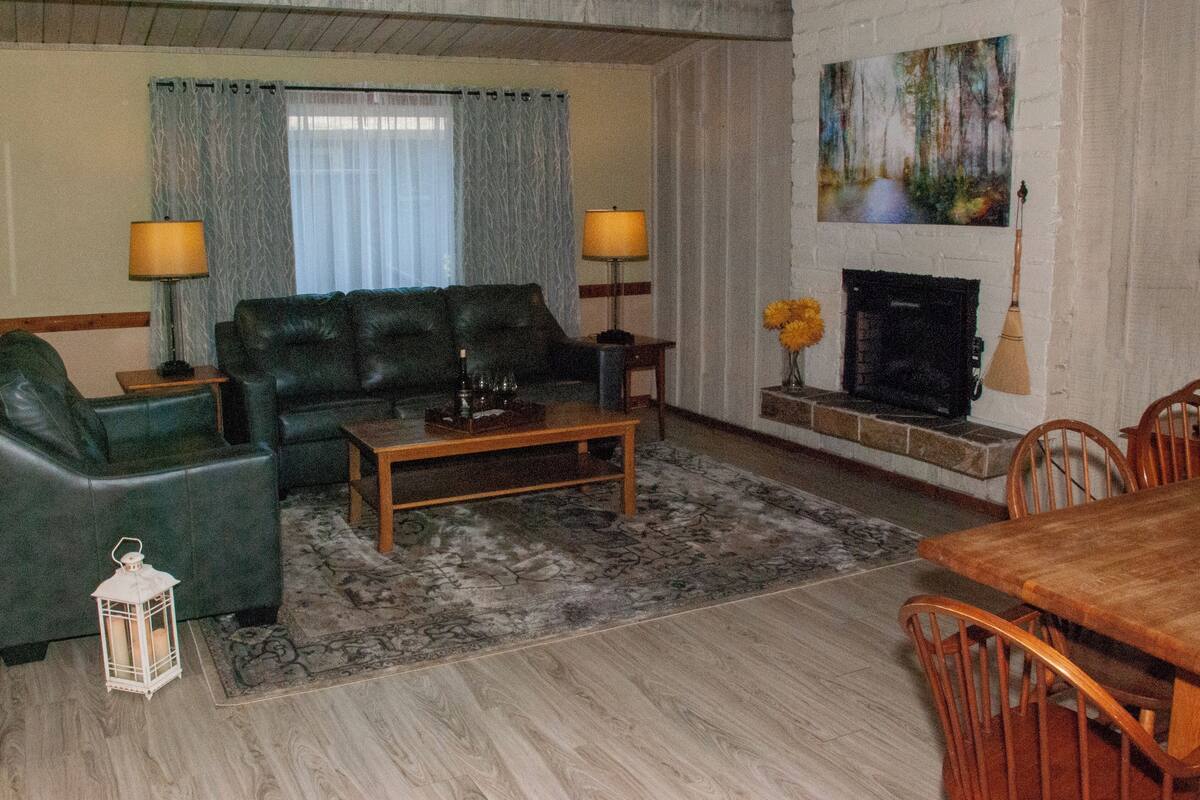A living room with a sofa, two armchairs, a coffee table, a fireplace, and a dining table with chairs.