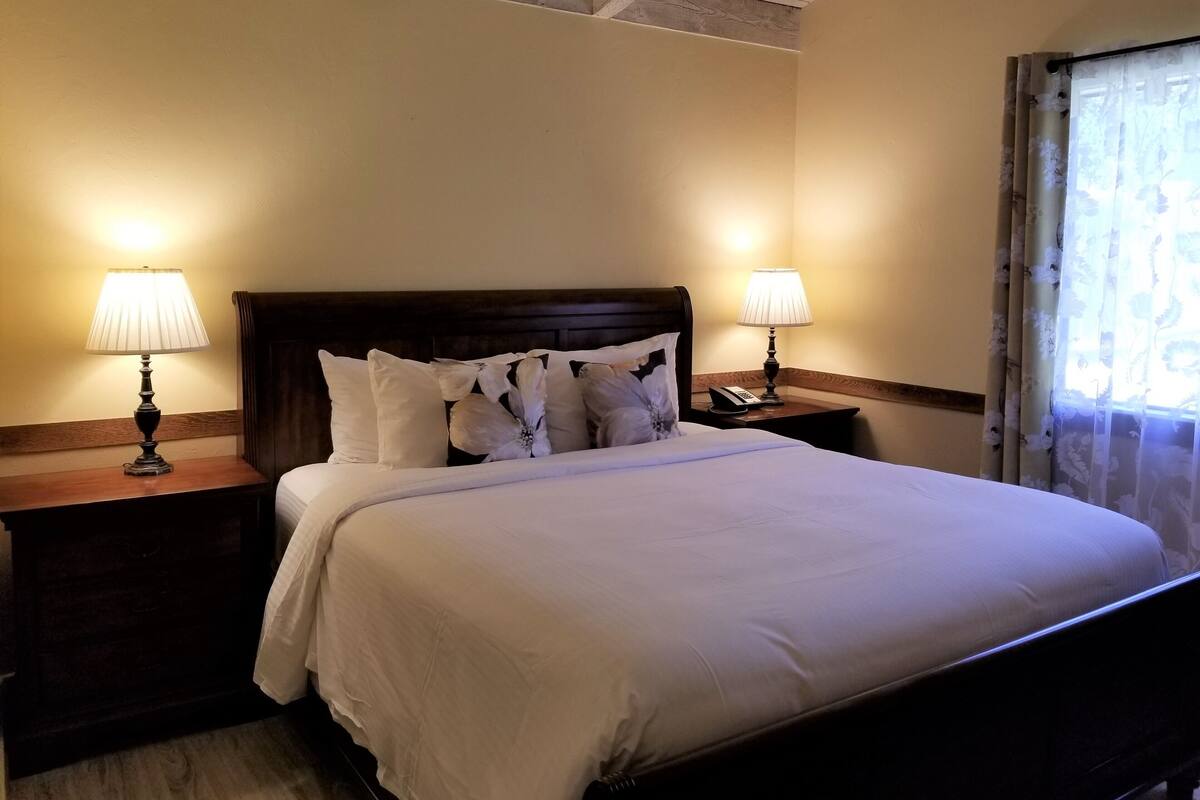 A neatly made bed with white bedding, two bedside tables with lamps, and a wooden headboard.