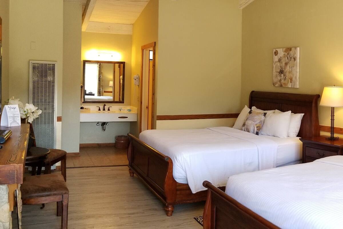 A hotel room with two beds, a desk, a mirror, and artwork on the walls.