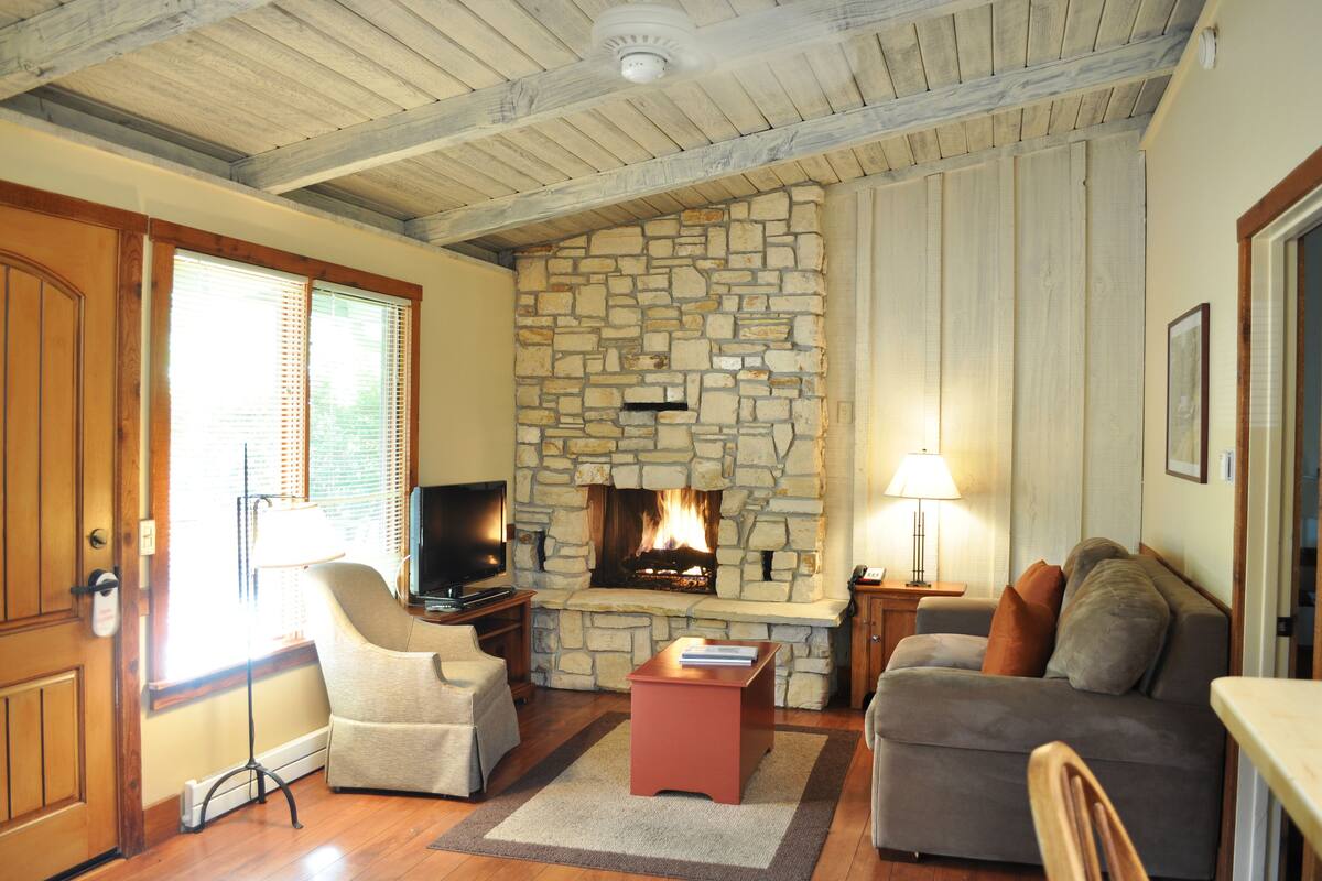 A cozy living room with a stone fireplace, wooden ceiling beams, and comfortable seating.