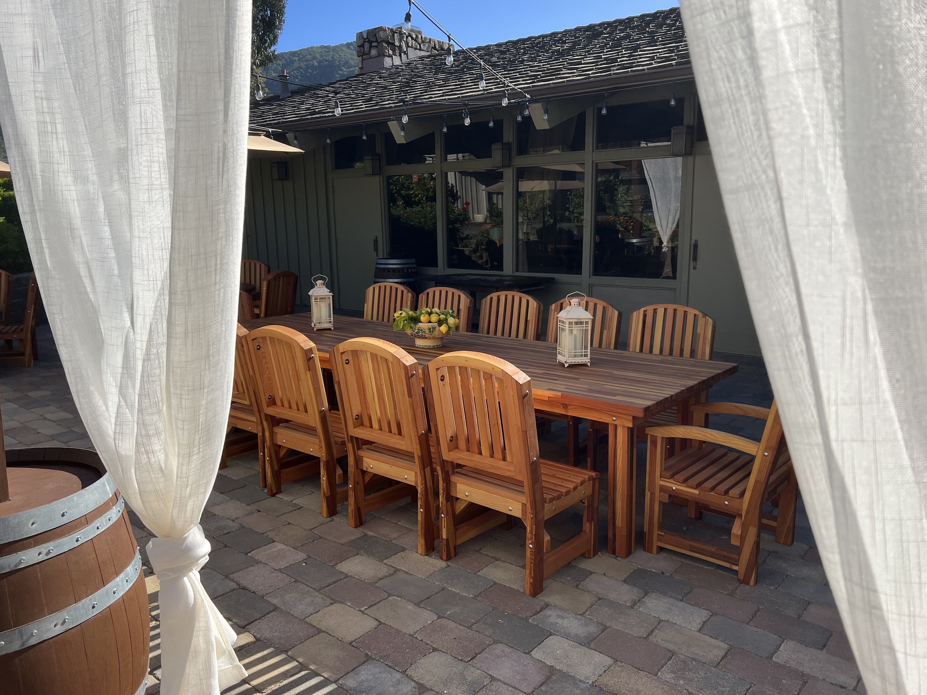 An outdoor patio with a wooden table and chairs, surrounded by white curtains.