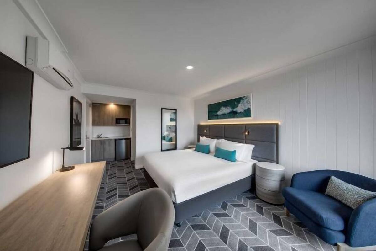 Een hotelkamer met een bed, een bureau, een stoel, een bank, een klein rond tafeltje en een kitchenette.