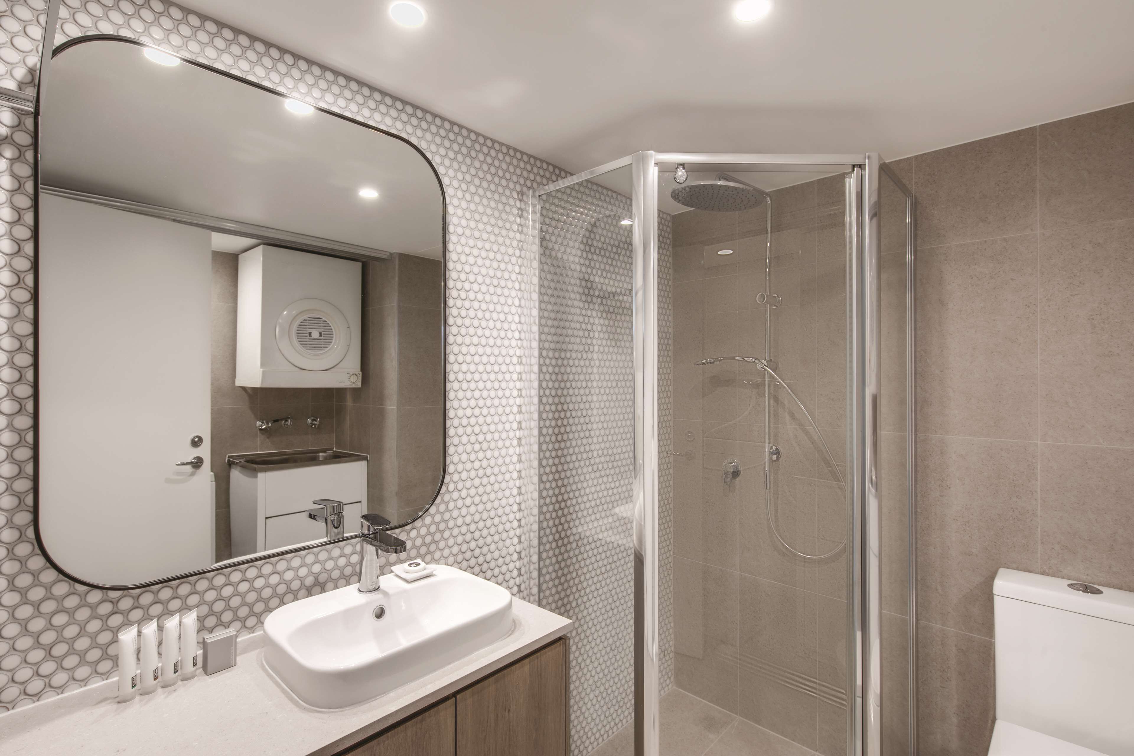 Un baño moderno con ducha envuelta en vidrio, un espejo grande y un lavamanos blanco.